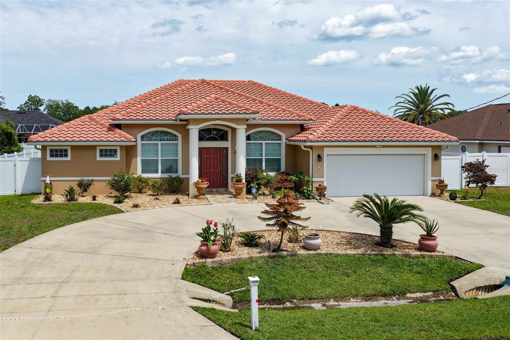 A single-story house with a terracotta tile roof, beige stucco walls, and a concrete driveway — 7 FLINT HILL LANE, PALM COAST, FL