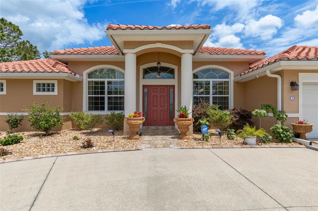 The exterior of a single-story house features a red tile roof and a central entryway — 7 FLINT HILL LANE, PALM COAST, FL