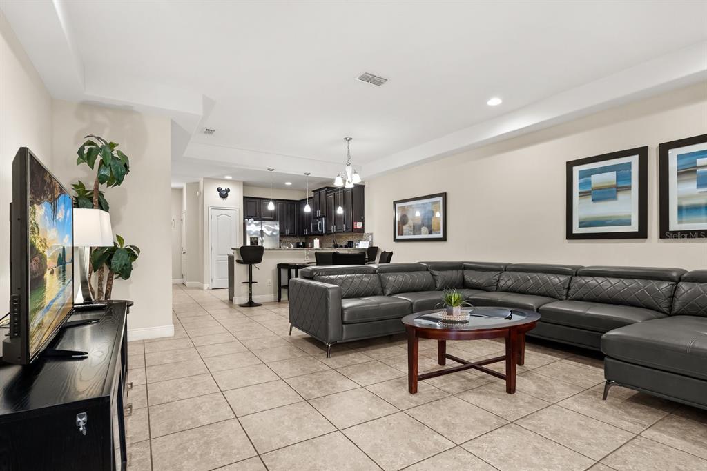 A living room with tile floors, a gray sectional sofa, and an open kitchen beyond — 8193 ROSEVILLE BOULEVARD, DAVENPORT, FL