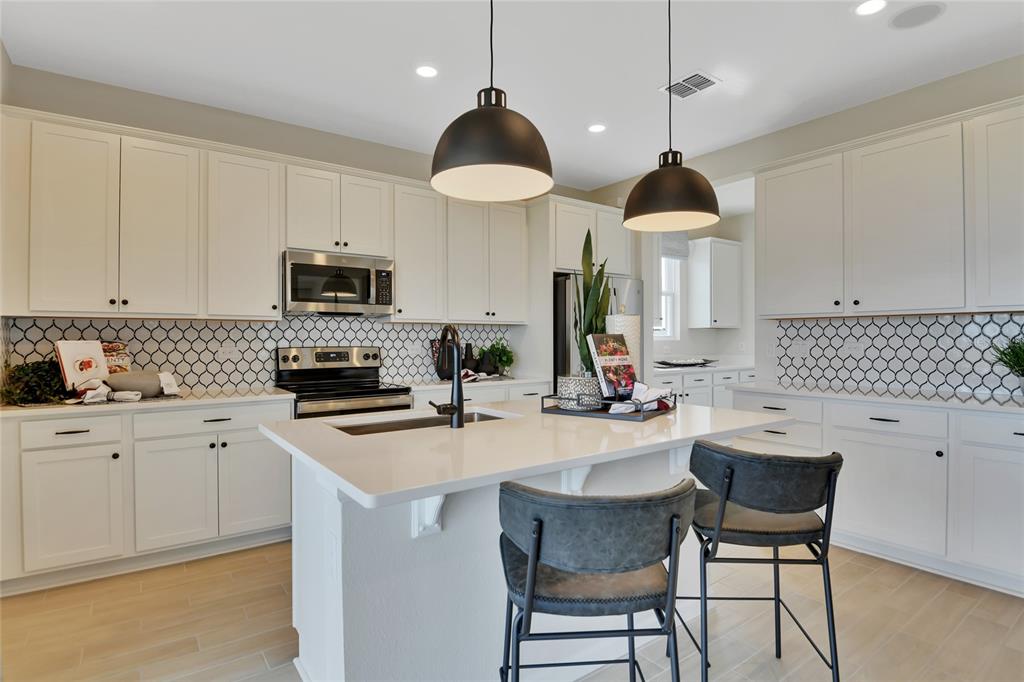 A kitchen features white cabinets, a central island with bar stools, and patterned tile backsplash — 14514 BANKS COURT, PARRISH, FL