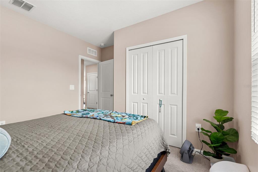 A bedroom features a bed with a gray quilt, white closet doors, and a potted plant — 5863 LE MARIN WAY, KISSIMMEE, FL