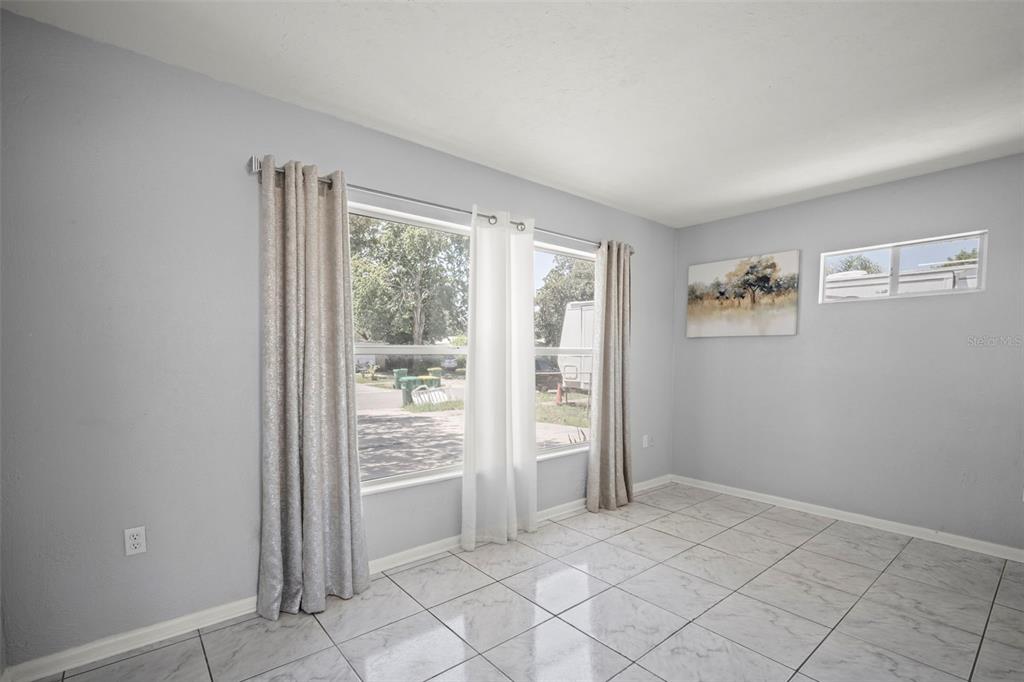 A bright room features light gray walls, white tile flooring, and a large window — 1010 ILLINOIS ROAD, COCOA, FL