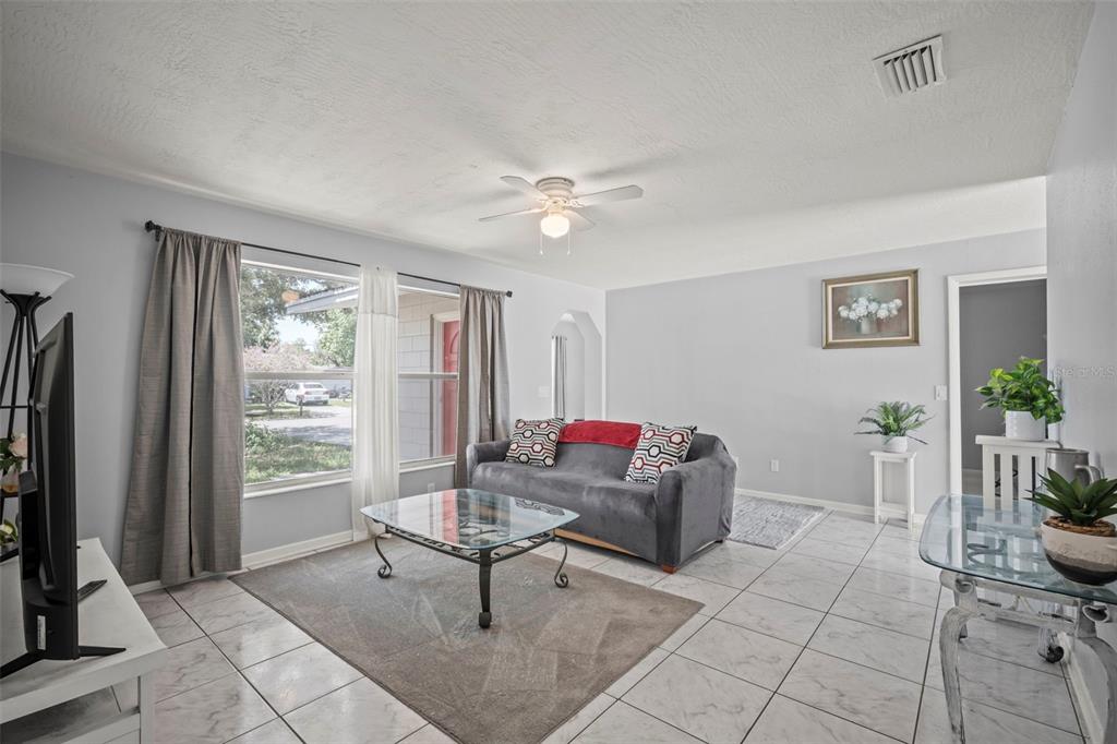 A living room with light gray walls, tile flooring, a gray sofa, and large windows — 1010 ILLINOIS ROAD, COCOA, FL