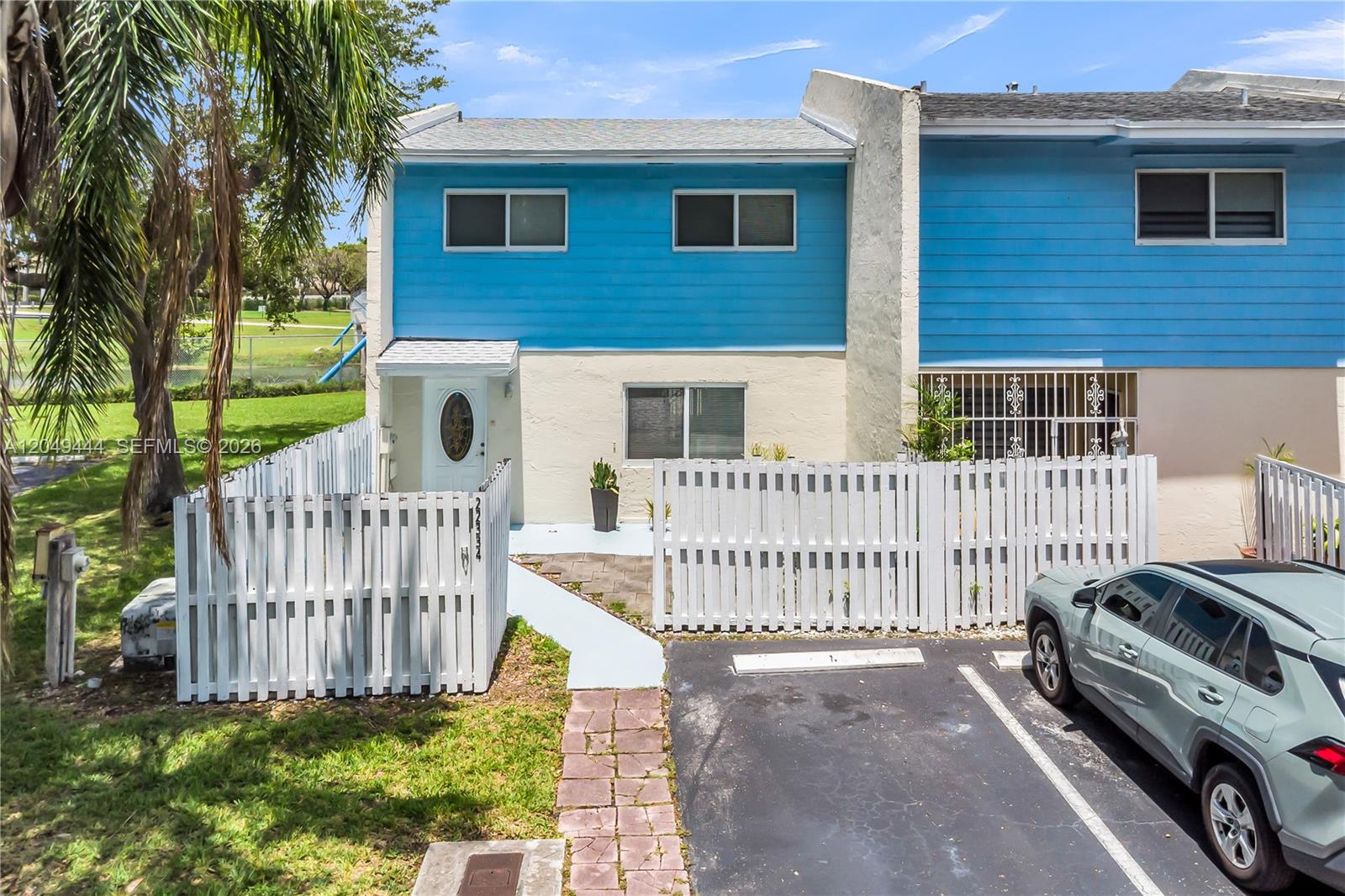A two-story townhouse with blue and beige siding features a white fence and driveway — 22334 SW 103rd Ct, Cutler Bay FL 33190, CUTLER BAY, FL