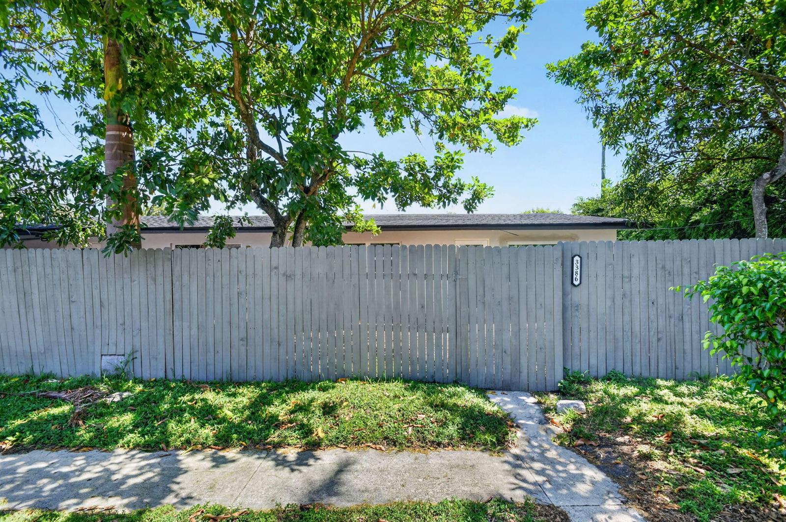 A wooden fence stands in front of a house with a tree and sidewalk — 3382 Rudolf Road, Lake Worth FL 33461, LAKE WORTH, FL