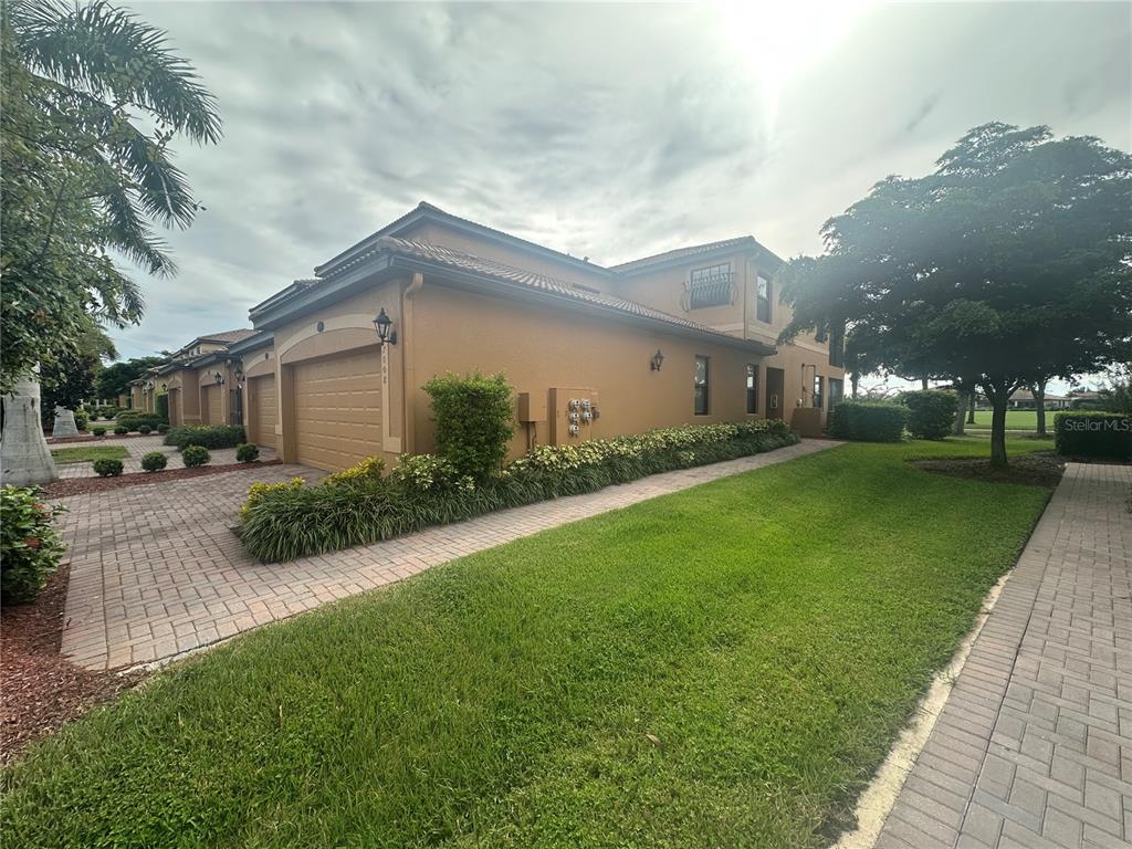 A two-story tan stucco townhouse features a brick paver driveway and a green lawn — 7008 GRAND ESTUARY TRAIL UNIT 104, BRADENTON, FL