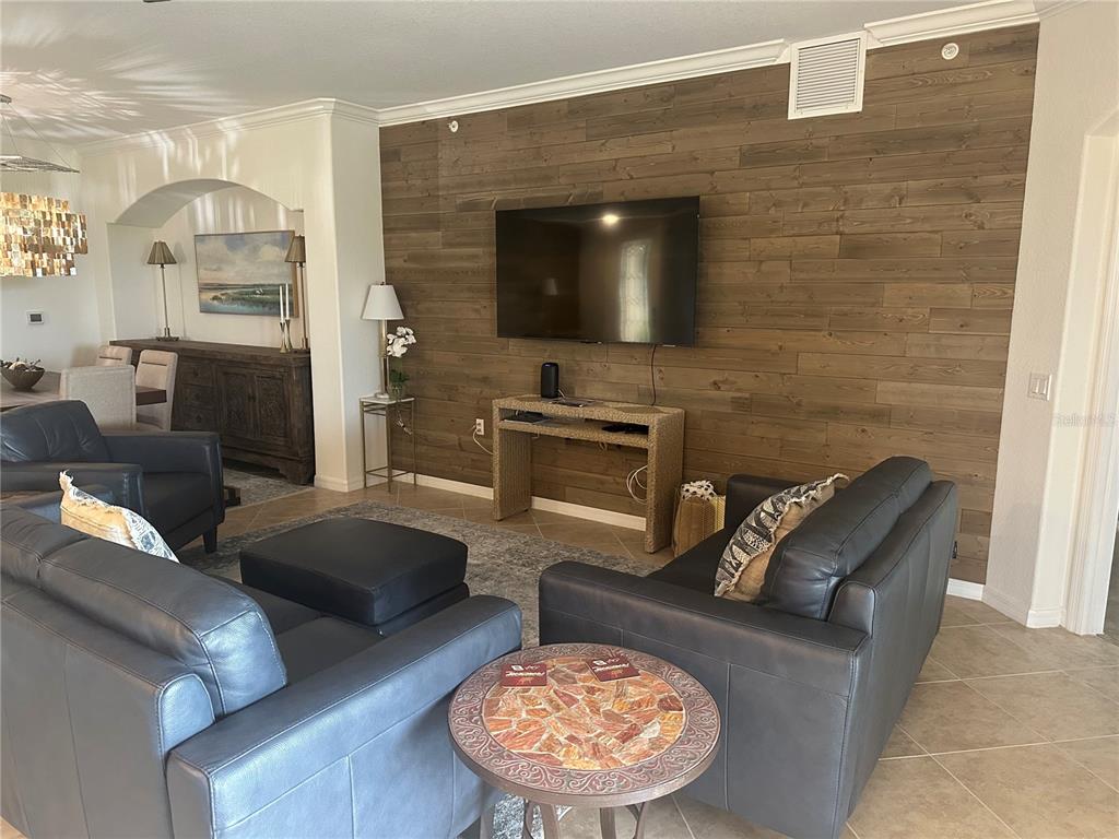 A living room features a wood-plank accent wall with a mounted television and leather furniture — 7008 GRAND ESTUARY TRAIL UNIT 104, BRADENTON, FL