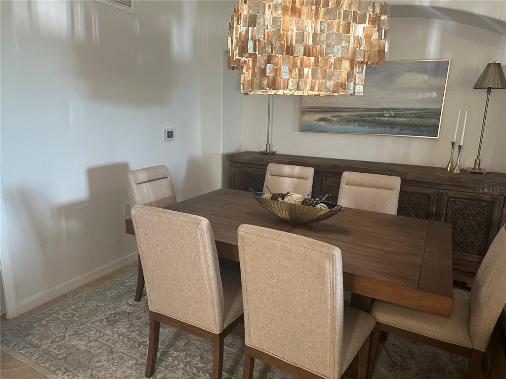 A dining room features a wooden table, upholstered chairs, a large chandelier, and a sideboard — 7008 GRAND ESTUARY TRAIL UNIT 104, BRADENTON, FL