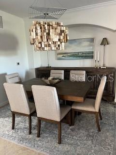 A dining room features a wooden table, six upholstered chairs, and a textured pendant light — 7008 GRAND ESTUARY TRAIL UNIT 104, BRADENTON, FL