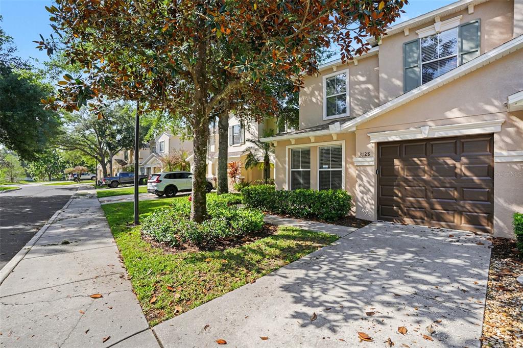 A two-story tan townhouse with a brown garage door and a tree-lined front yard — 3128 ROYAL TUSCAN LANE, VALRICO, FL