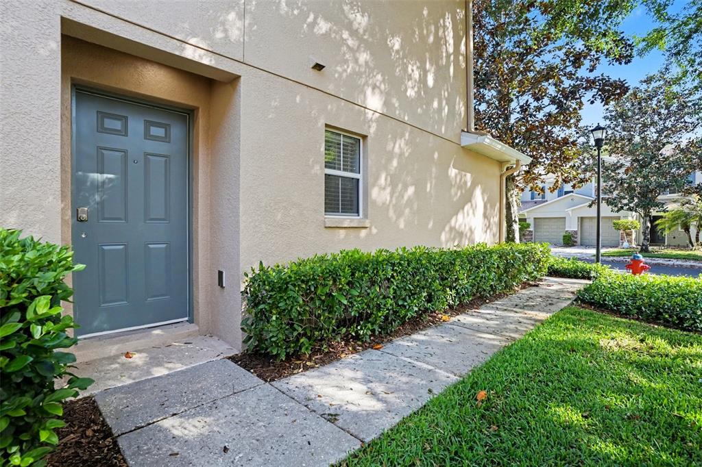 A gray front door is set into a beige stucco building beside a concrete walkway — 3128 ROYAL TUSCAN LANE, VALRICO, FL