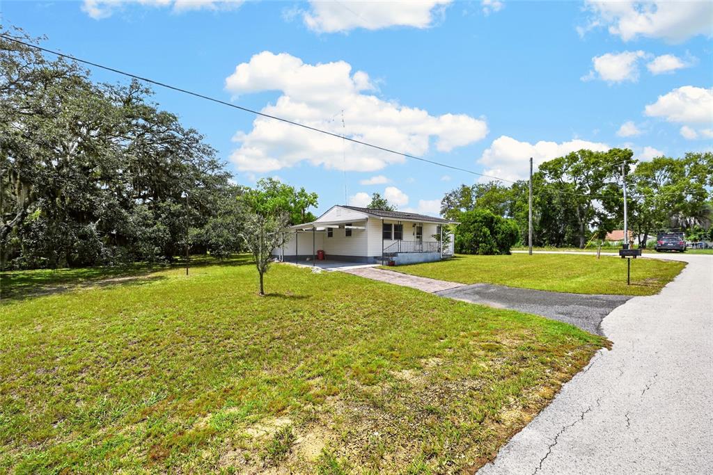 A small, white, single-story house with a carport sits on a large, grassy lot — 16220 SE 83RD COURT, SUMMERFIELD, FL