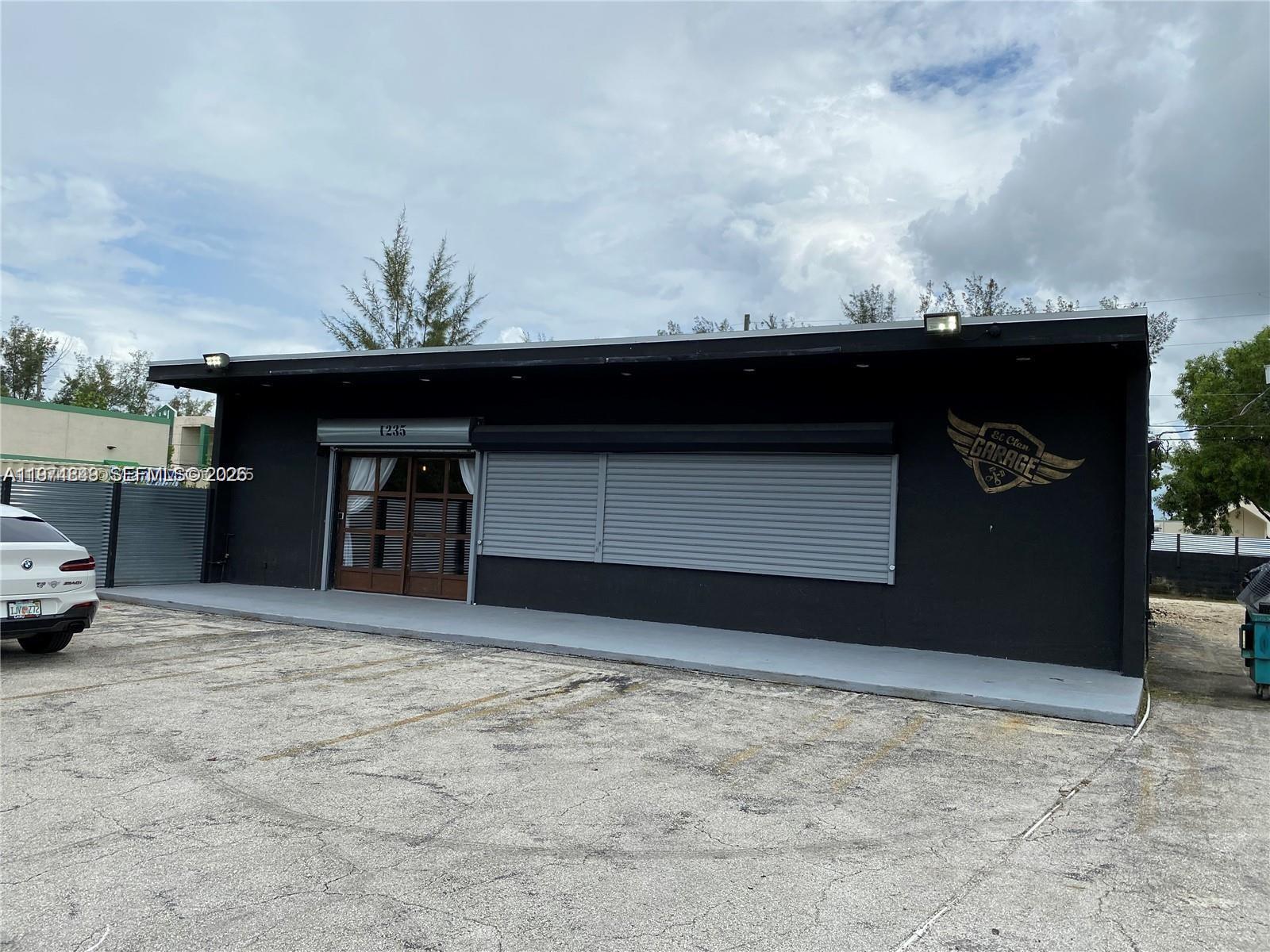 A black commercial building with a gray roll-down shutter and a parking lot in front — 1235 NW 103rd St, Miami FL 33147, MIAMI, FL