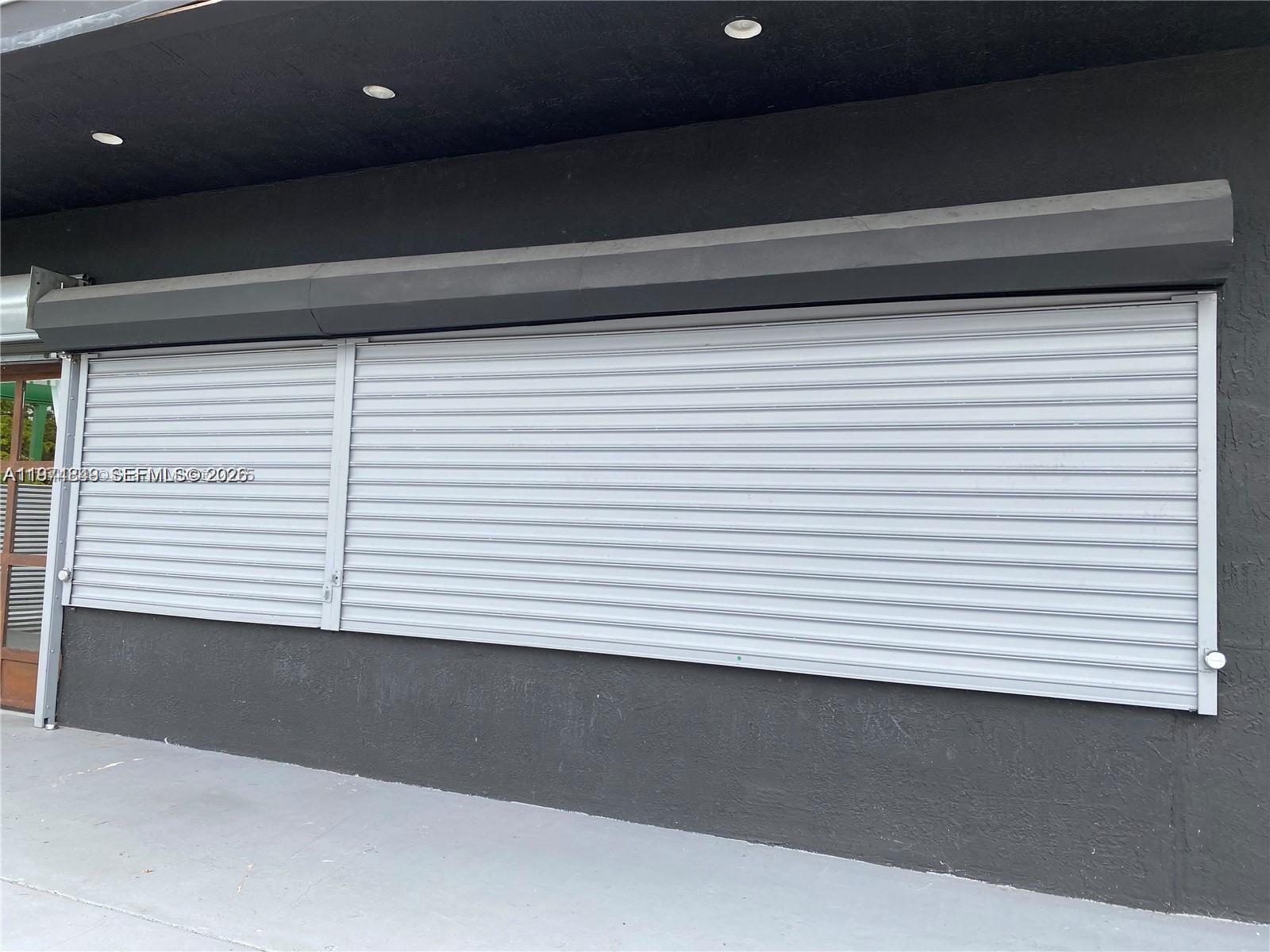 A storefront exterior features a large window covered by gray metal security shutters — 1235 NW 103rd St, Miami FL 33147, MIAMI, FL