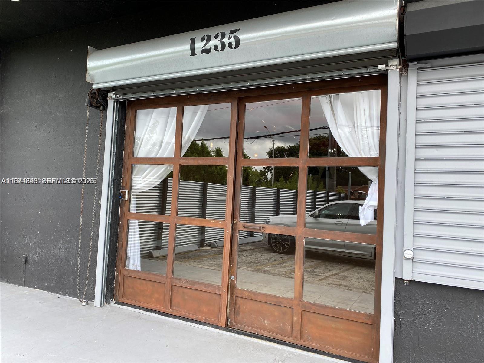 A storefront entrance features a metal roll-down door above a brown-framed glass door with curtains — 1235 NW 103rd St, Miami FL 33147, MIAMI, FL