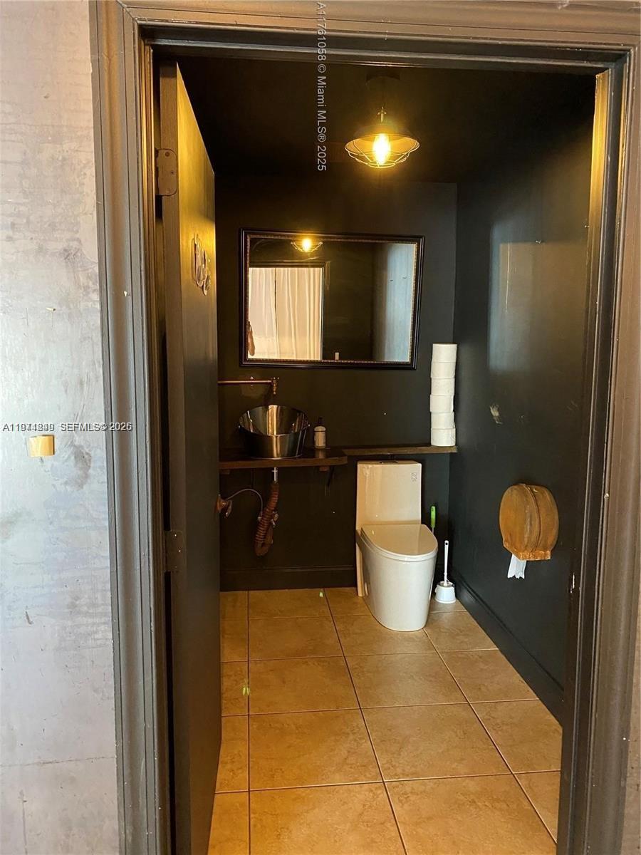 A small bathroom features dark walls, a vessel sink, a toilet, and tile flooring — 1235 NW 103rd St, Miami FL 33147, MIAMI, FL