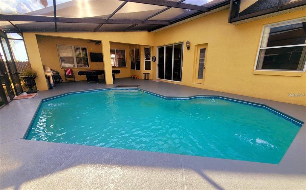 A swimming pool sits on a patio enclosed by a screened lanai behind a house — 10 NEVADA LOOP ROAD, DAVENPORT, FL