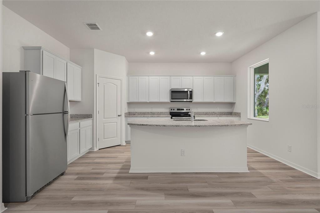 A kitchen features white cabinetry, granite countertops, a center island, and stainless steel appliances — 306 BOWFIN COURT, POINCIANA, FL