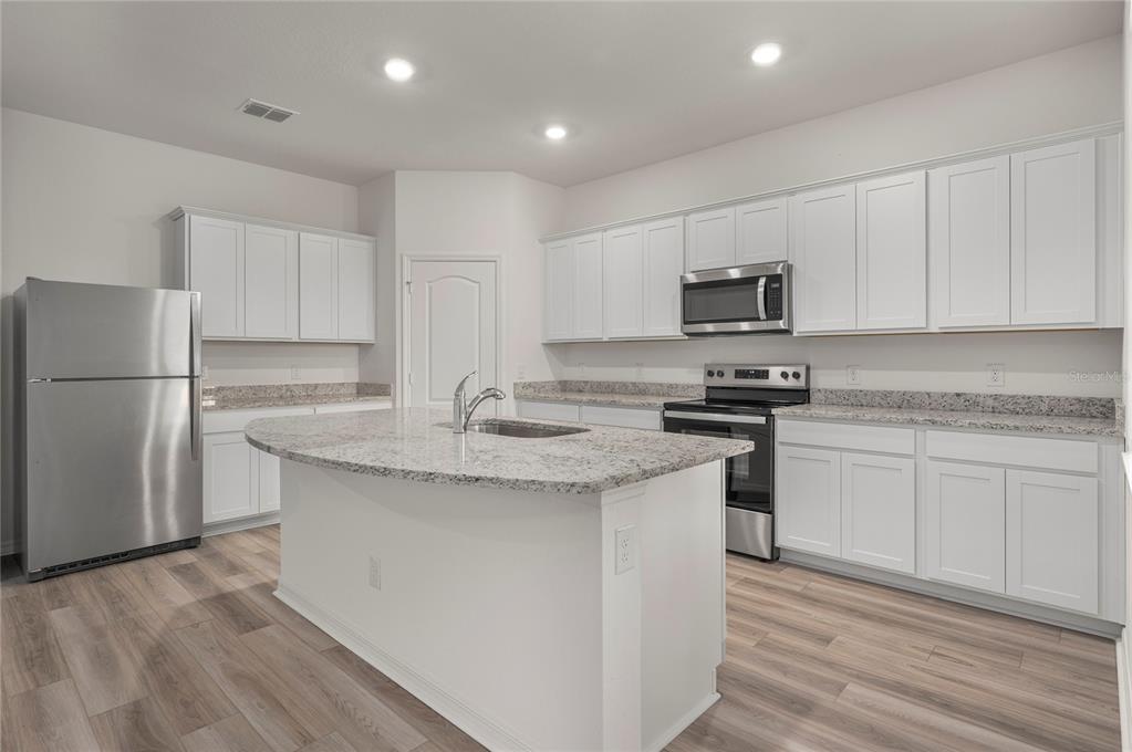 A kitchen with white cabinets, granite countertops, stainless steel appliances, and a central island — 306 BOWFIN COURT, POINCIANA, FL