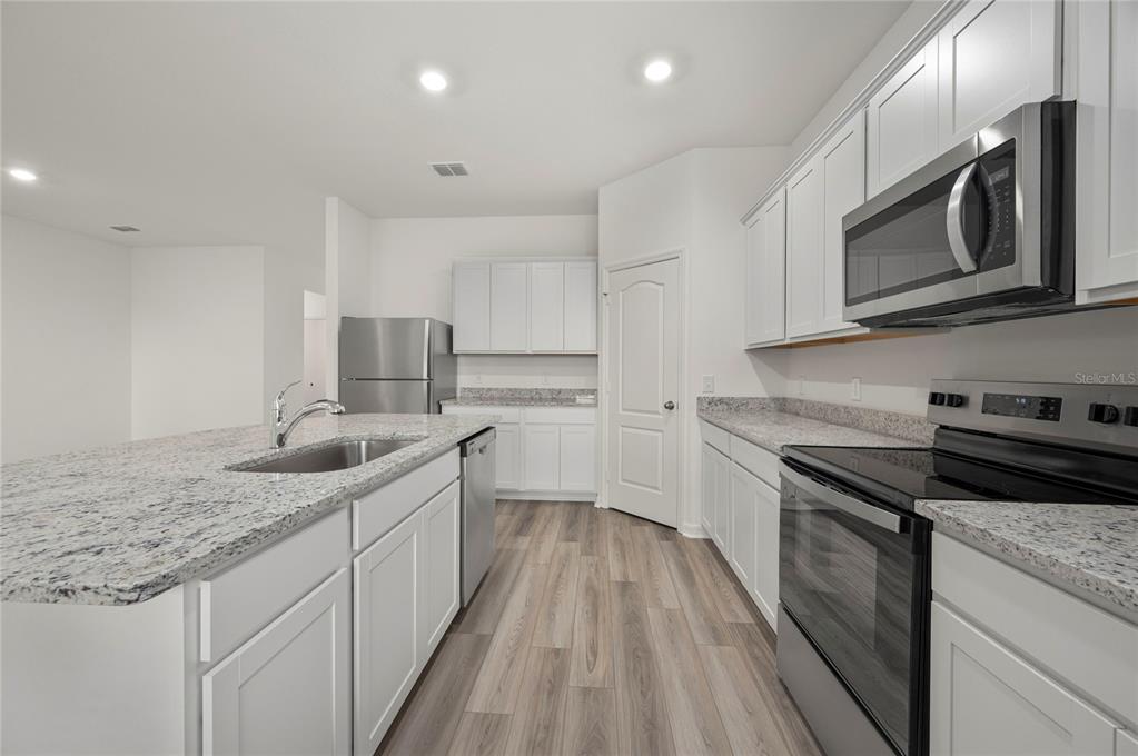 A kitchen with white cabinets, granite countertops, stainless steel appliances, and wood-look flooring — 306 BOWFIN COURT, POINCIANA, FL