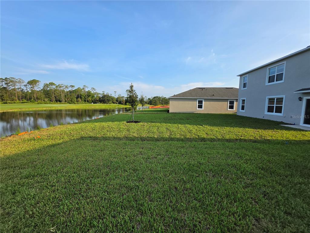 A grassy backyard overlooks a pond with neighboring houses visible in the background — 1013 CHAMPION RIDGE DRIVE, DAYTONA BEACH, FL
