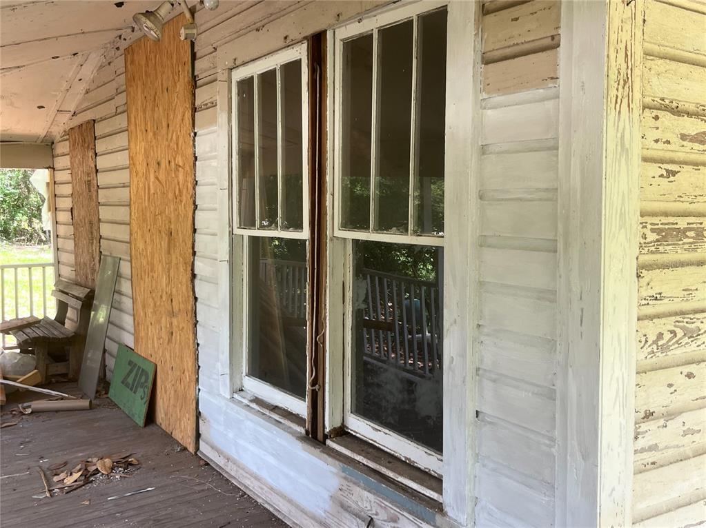A weathered porch features peeling white siding, two double-hung windows, and a plywood-covered wall section — 10033 SW COUNTY ROAD 225, STARKE, FL