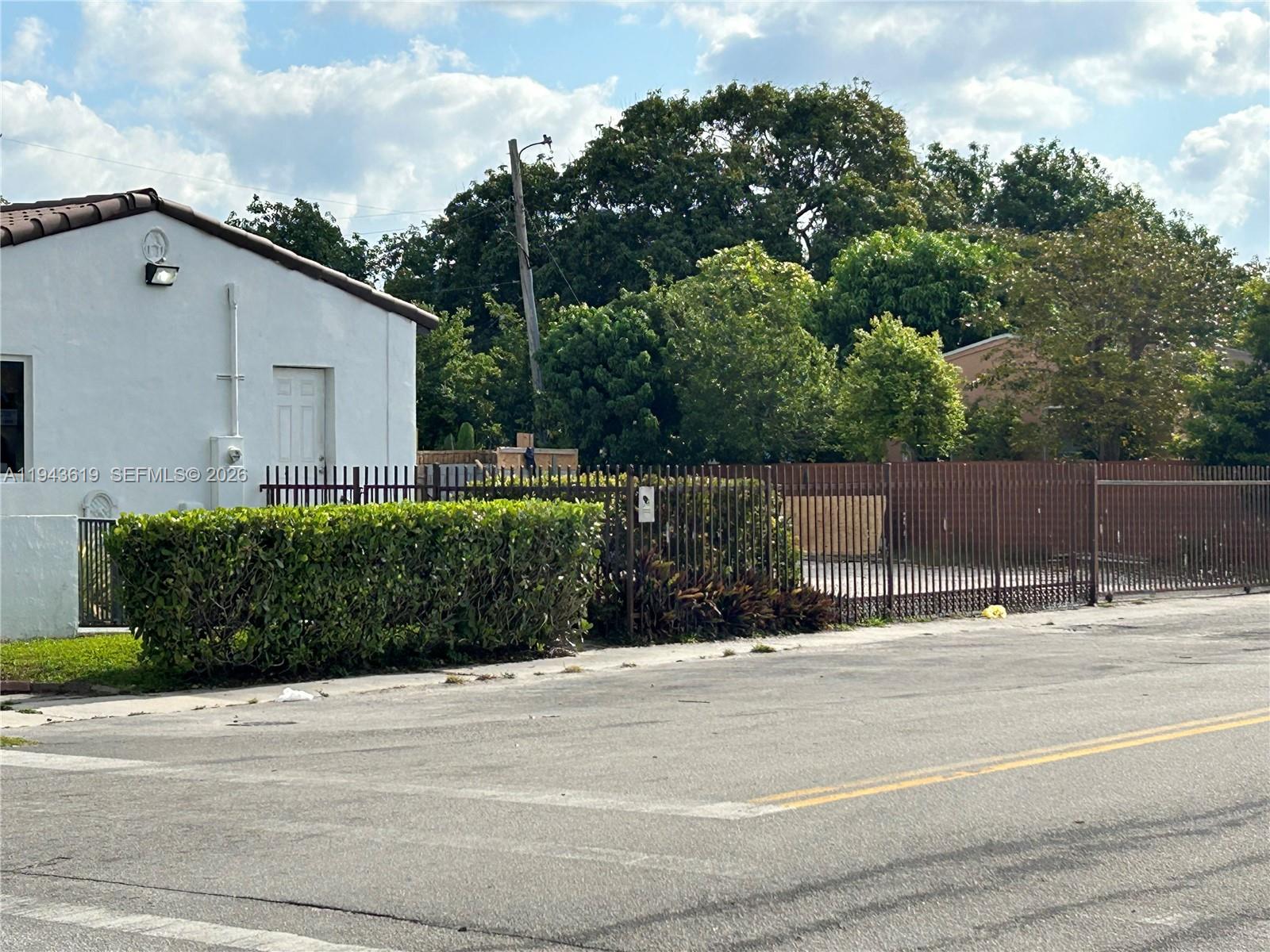 A white building with a brown roof sits behind a tall metal fence and hedge — 3521 E 4th Ave, Hialeah FL 33013, HIALEAH, FL