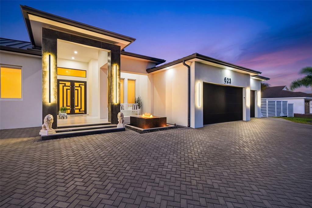 A modern house exterior features a paved driveway, a fire pit, and a grand entryway — 523 SW 23RD STREET, CAPE CORAL, FL