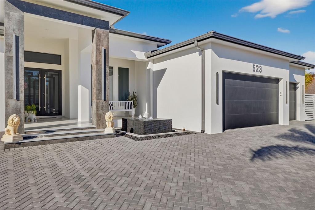 A modern white house exterior features a paved driveway, a garage, and a small fountain — 523 SW 23RD STREET, CAPE CORAL, FL