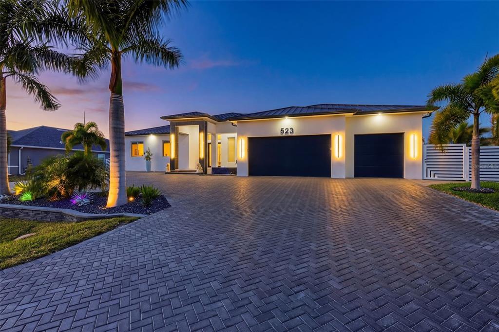 A modern single-story house with a paved driveway, dark garage doors, and palm trees at dusk — 523 SW 23RD STREET, CAPE CORAL, FL