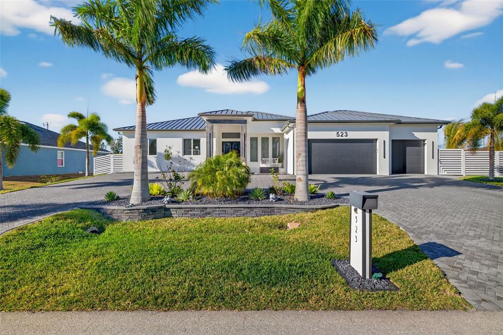 A modern, single-story house with a paved driveway, two palm trees, and a dark garage — 523 SW 23RD STREET, CAPE CORAL, FL