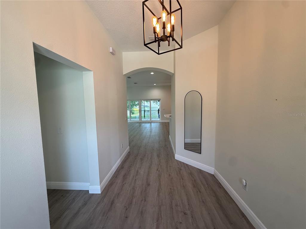 A foyer with wood-look flooring, a geometric pendant light, and an arched entryway — 16382 SE 83RD AVENUE, SUMMERFIELD, FL