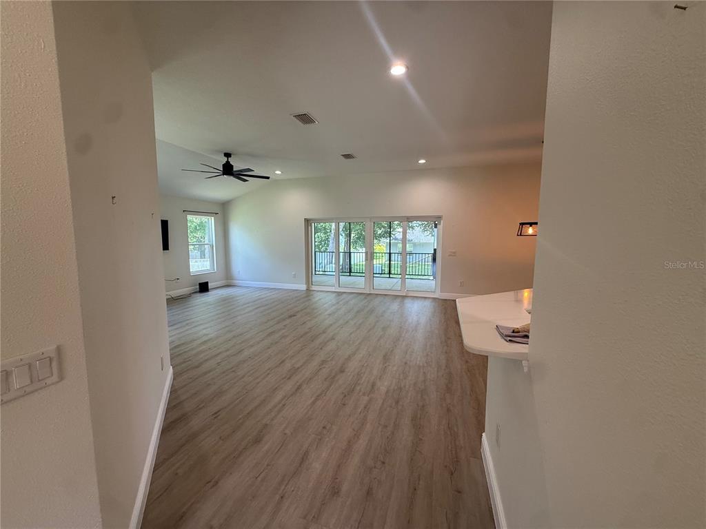 An open-concept living area features light wood-look flooring, a ceiling fan, and sliding glass doors — 16382 SE 83RD AVENUE, SUMMERFIELD, FL