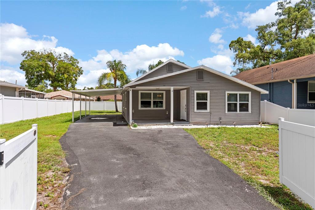 A gray, single-story house with a carport and a white vinyl fence in the front yard — 1804 E IDLEWILD AVENUE, TAMPA, FL