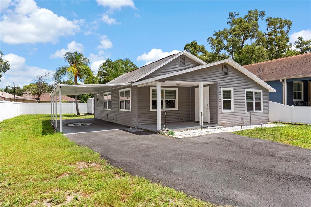A gray, single-story house with a carport, asphalt driveway, and white vinyl fencing — 1804 E IDLEWILD AVENUE, TAMPA, FL