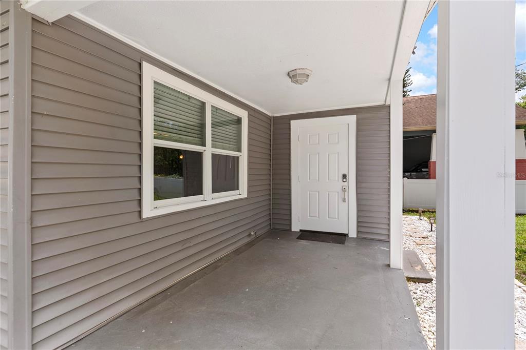 A covered concrete porch features gray horizontal siding, a white front door, and a window — 1804 E IDLEWILD AVENUE, TAMPA, FL