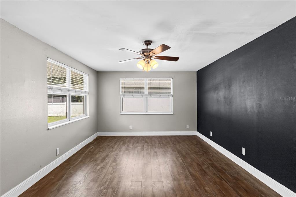 An empty room features wood-look flooring, a ceiling fan, and a black accent wall — 1804 E IDLEWILD AVENUE, TAMPA, FL