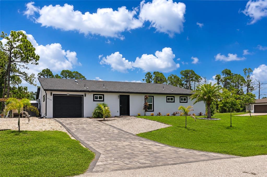 A single-story white house with a black garage door and a paved driveway — 1458 E HALLMARK BOULEVARD, NORTH PORT, FL