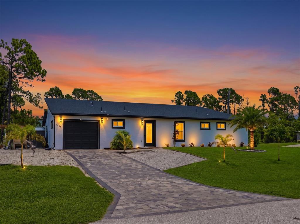 A single-story house with a paved driveway, black garage door, and white exterior at sunset — 1458 E HALLMARK BOULEVARD, NORTH PORT, FL
