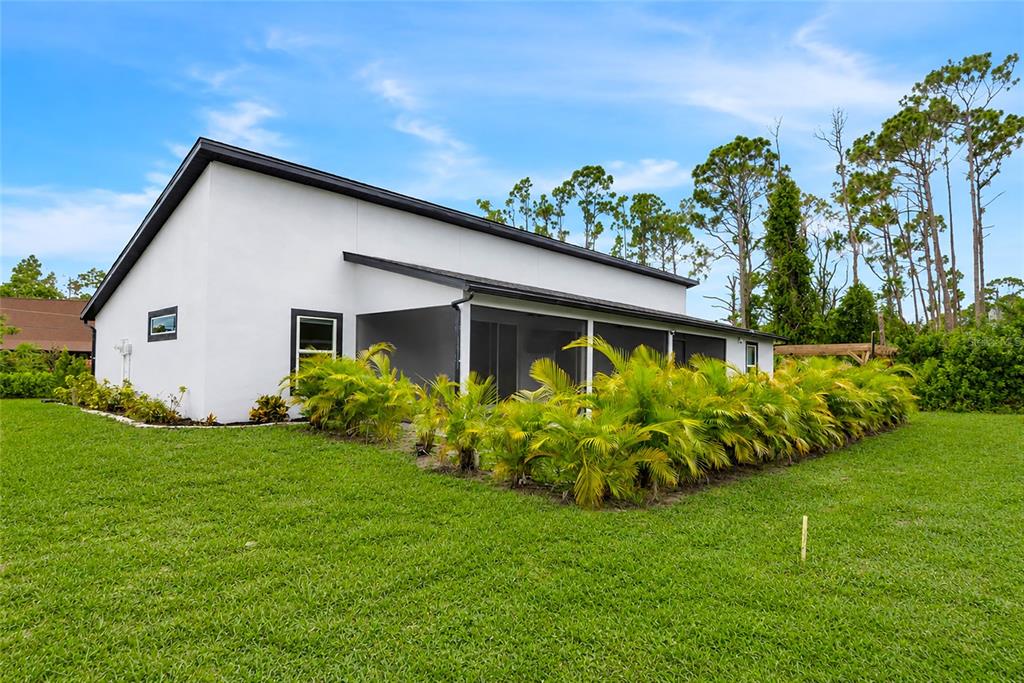 A white house exterior features a screened-in patio and a row of small palm trees — 1458 E HALLMARK BOULEVARD, NORTH PORT, FL