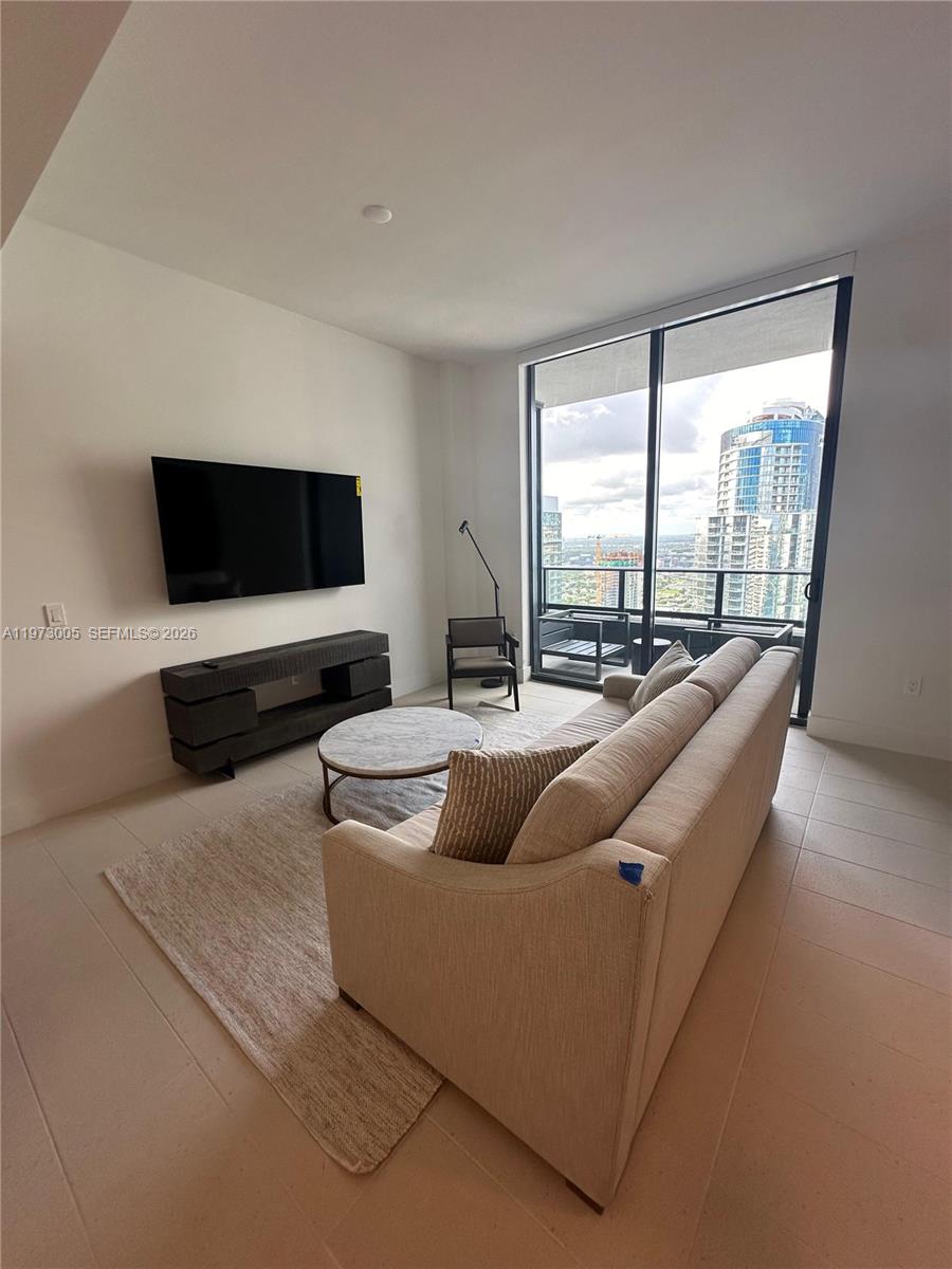 A modern living room features a beige sofa, circular coffee table, and floor-to-ceiling windows — 159 NE 6th St # 4811, Miami FL 33132, MIAMI, FL