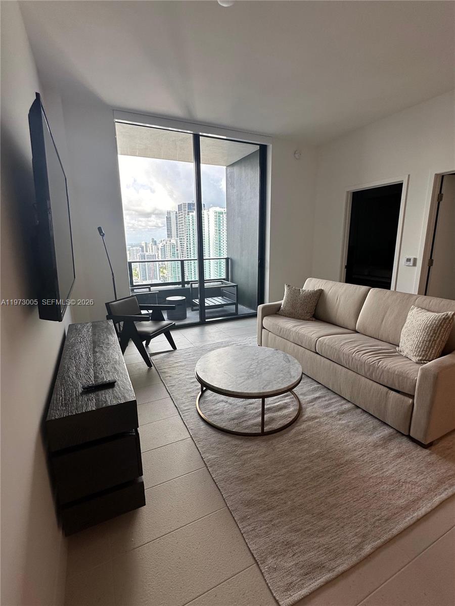 A modern living room features a sofa, coffee table, television, and a balcony with city views — 159 NE 6th St # 4811, Miami FL 33132, MIAMI, FL