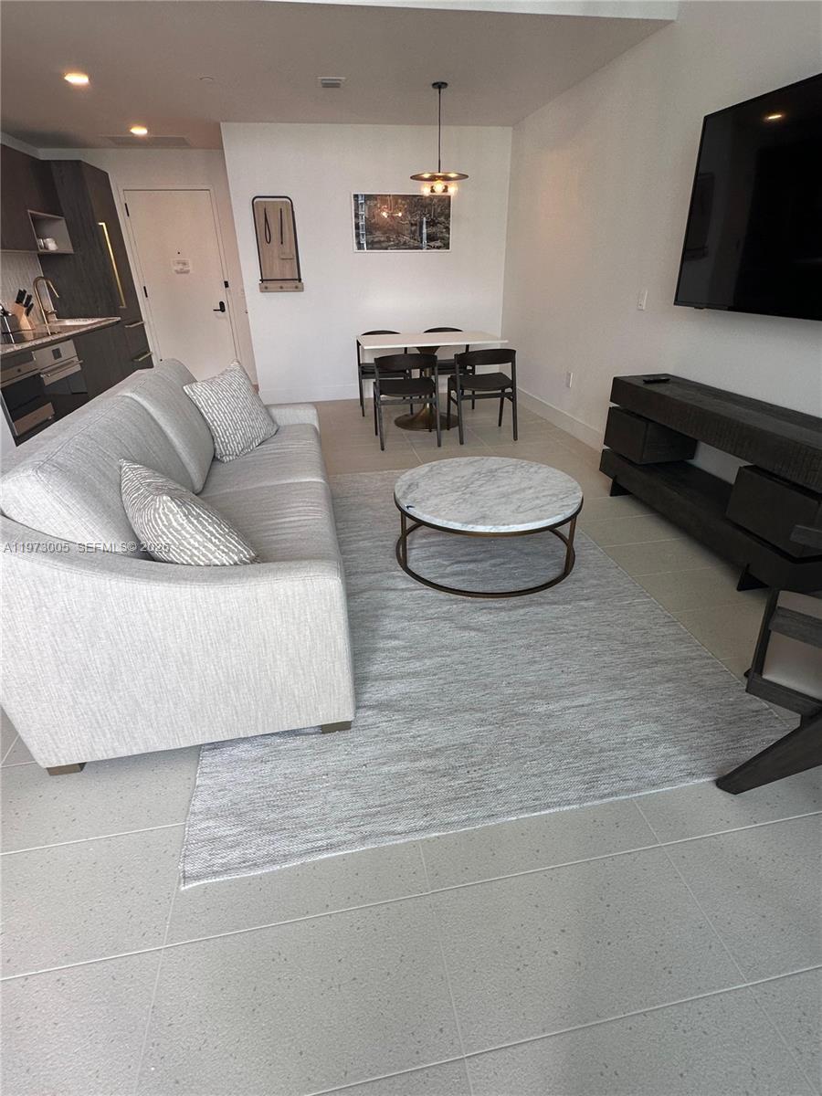 A modern living room features a gray sofa, a marble coffee table, and a dining area — 159 NE 6th St # 4811, Miami FL 33132, MIAMI, FL