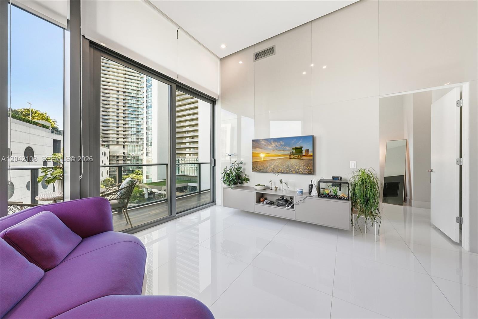 A modern living room features a purple sofa, white tile floors, and a balcony view — 501 NE 31st St # 401, Miami FL 33137, MIAMI, FL