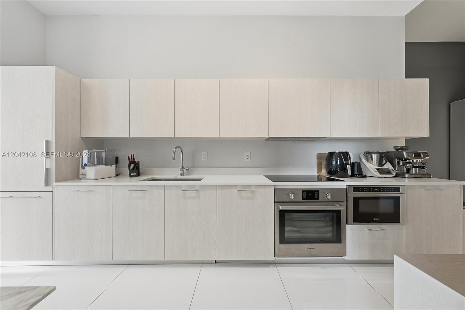 A modern kitchen features light wood cabinetry, stainless steel appliances, and white tile flooring — 501 NE 31st St # 401, Miami FL 33137, MIAMI, FL
