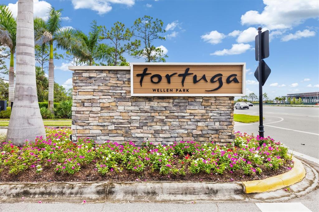 A stone monument sign for Tortuga at Wellen Park sits in a landscaped garden bed — 11125 BALFOUR STREET, VENICE, FL