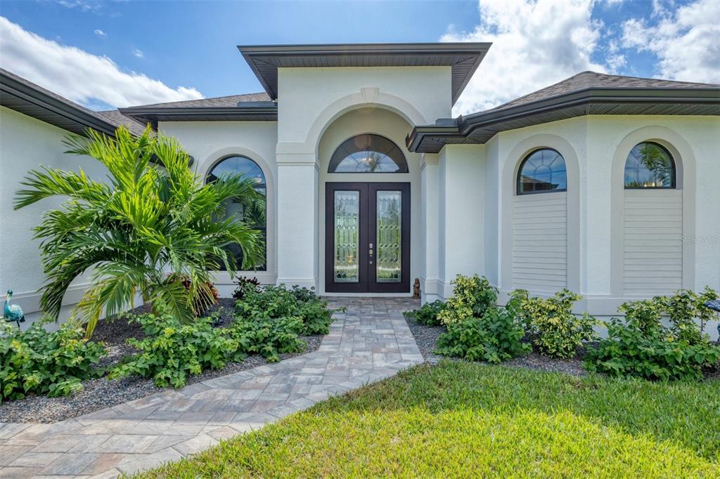 The exterior of a white house features a paved walkway leading to double front doors — 16660 LIGGETT CIRCLE, PORT CHARLOTTE, FL