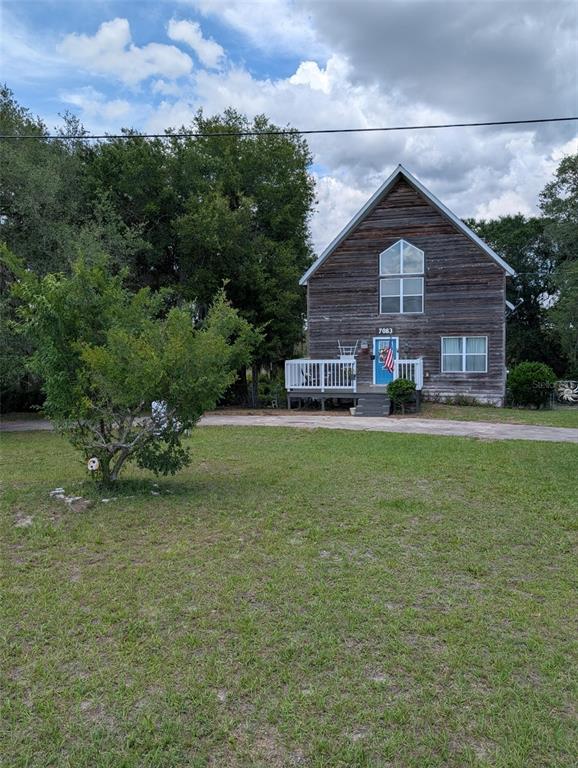 A two-story house with wood siding and a front deck sits on a grassy lot — 7083 SE 166TH AVENUE, OCKLAWAHA, FL