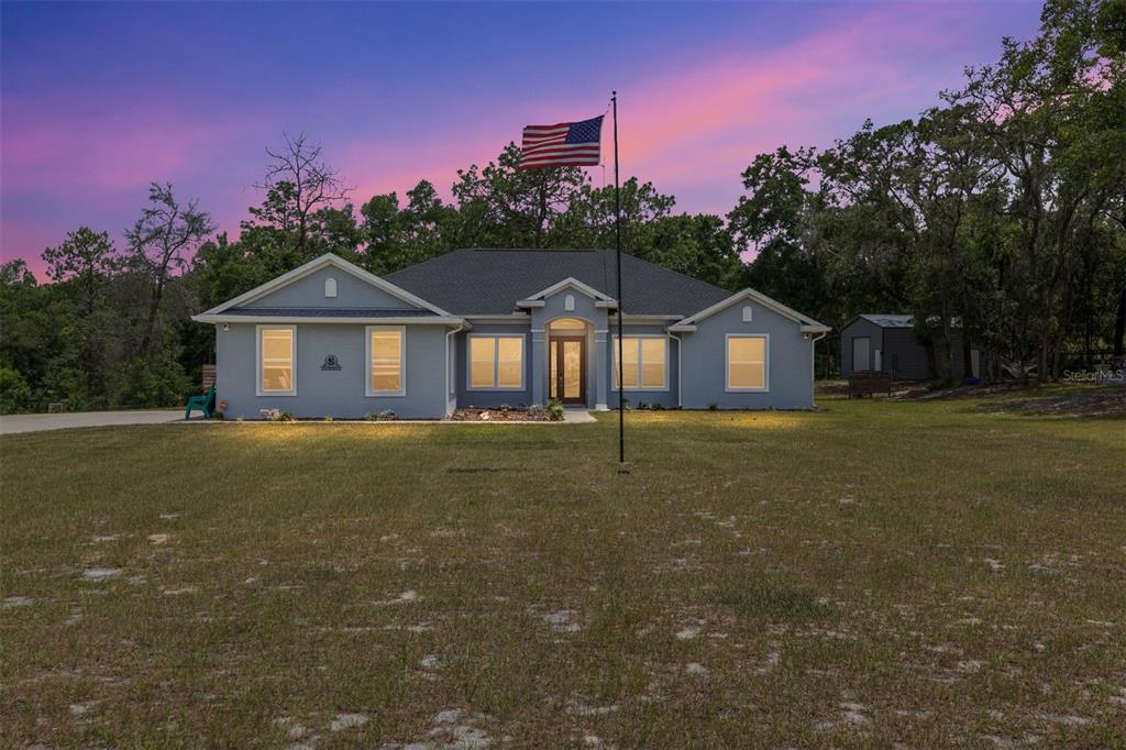 A single-story gray house with a flag pole stands on a grassy lot at dusk — 10254 SE 118TH LANE, BELLEVIEW, FL