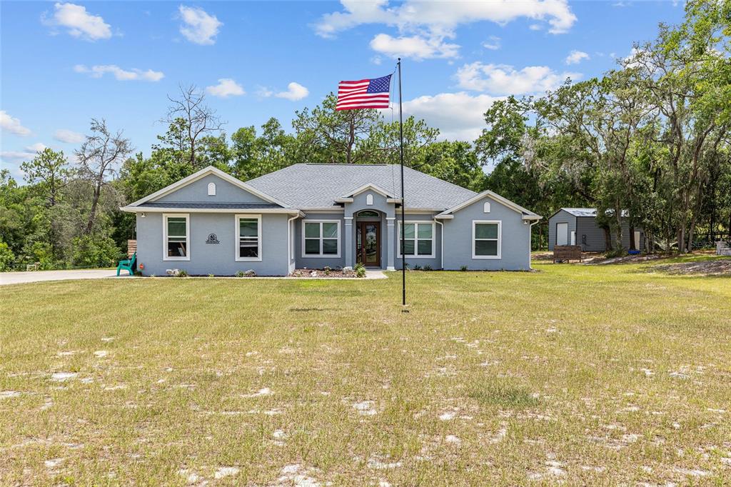 A single-story gray house with a front porch and an American flag in the yard — 10254 SE 118TH LANE, BELLEVIEW, FL